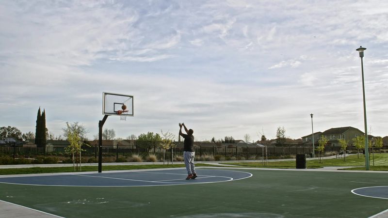 A person alone on a suburban park’s basketball court, shooting a basket.