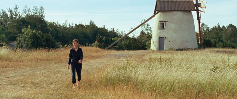 A woman walks in a field, a windmill in the background.