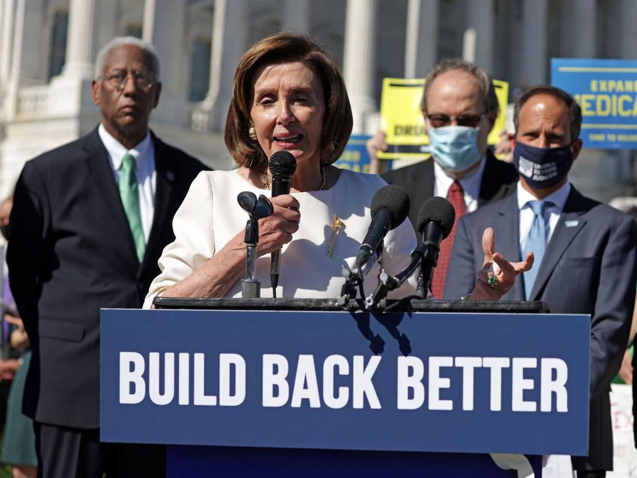 House Speaker Nancy Pelosi talks into a microphone at a lectern with a sign that reads, “Build Back Better.”