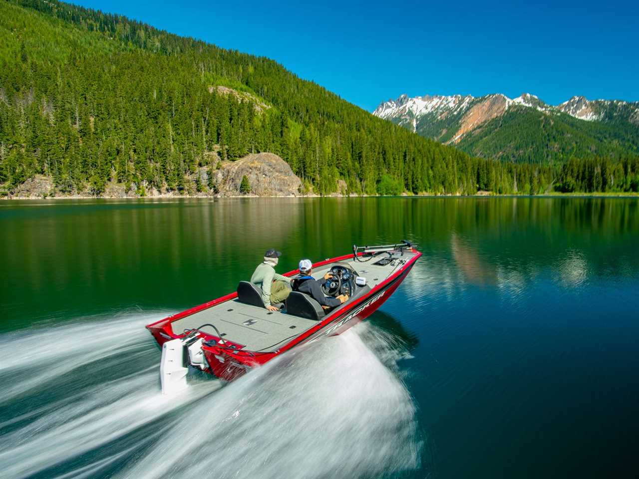 An electric speed boat zooming across a lake surrounded by forested hills.