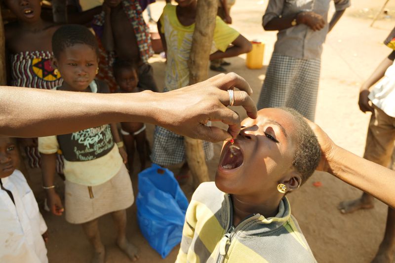 A child tilts their head back and opens their mouth so an adult hand can drop in a pill.