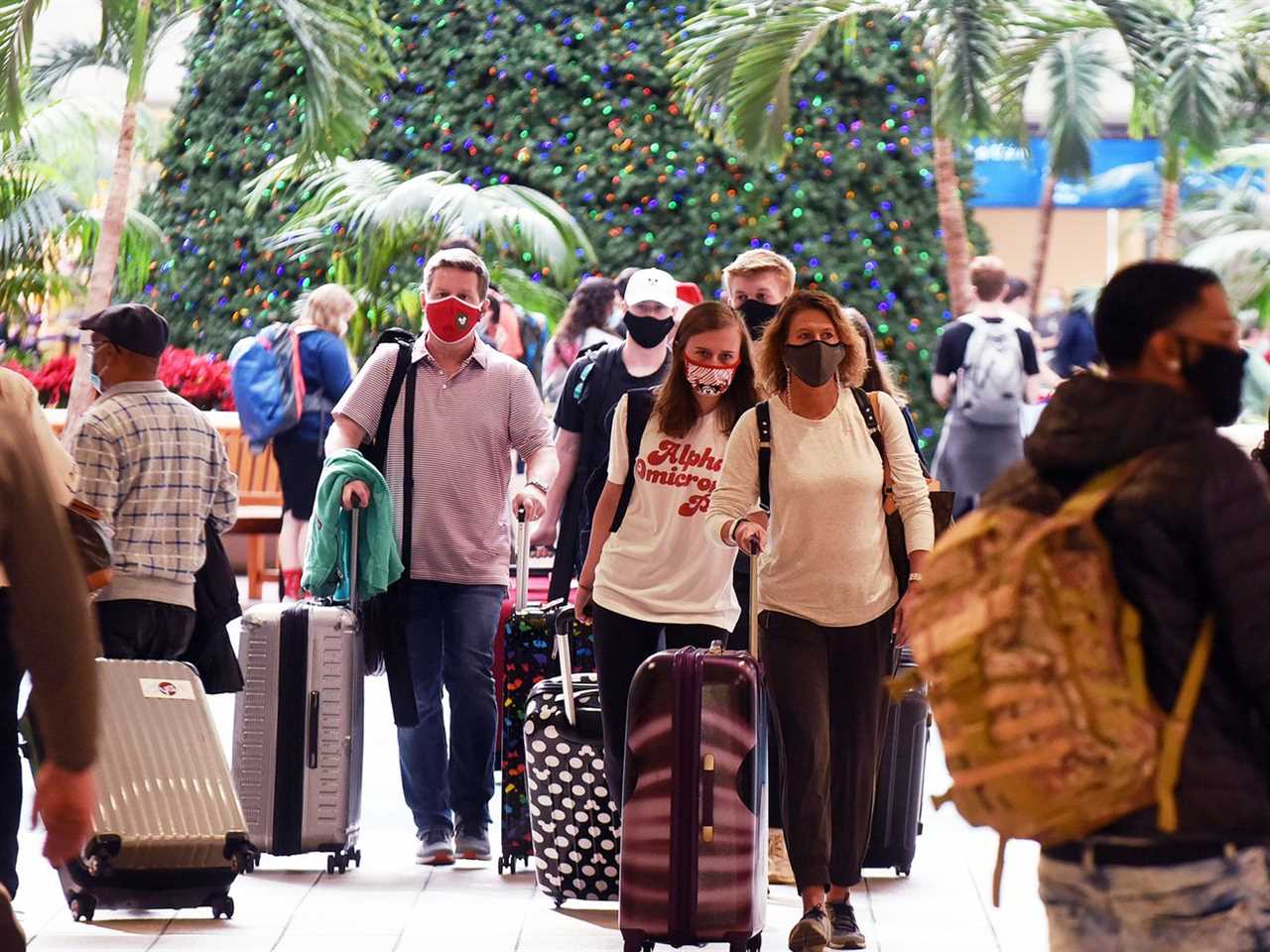 A crowd of people wearing masks and rolling luggage through an airport.