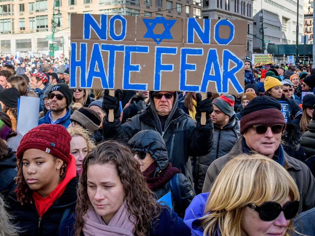 A crowd of people in the Manhattan streets hold signs including “No Hate, No Fear.”