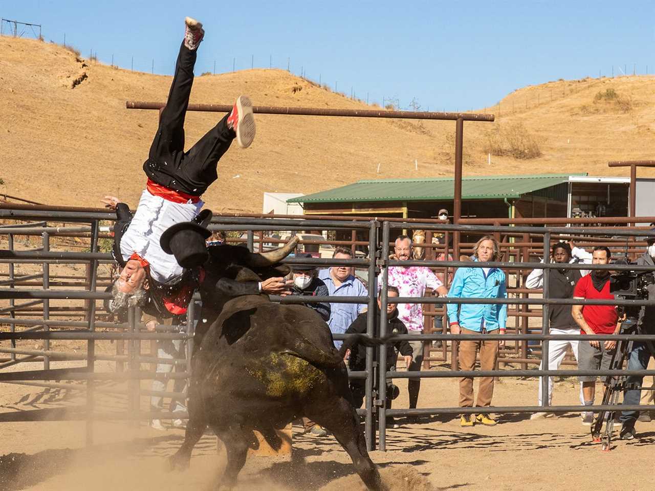 A man in a tuxedo is flying through the air upside down, having been flipped over by a bull in a ring.