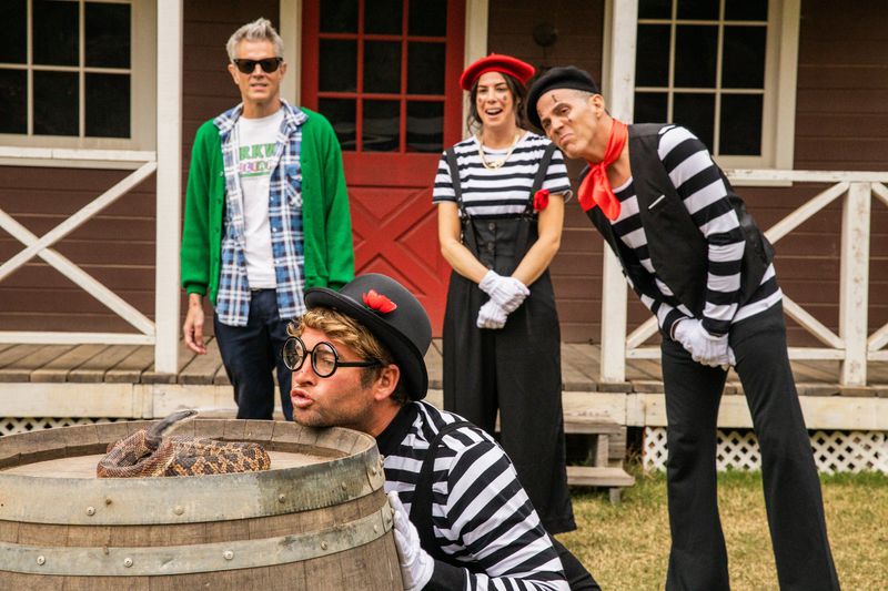 Three people in mime costumes and Johnny Knoxville watch as one of the mimes puckers up at a snake.