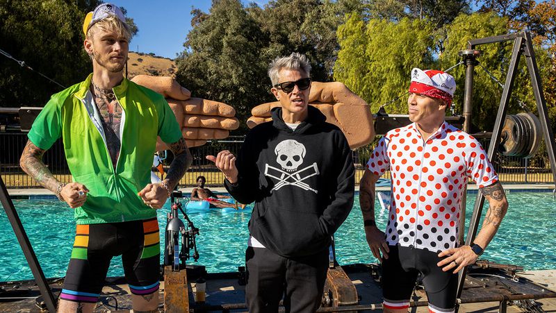 Three guys in weird clothes stand in front of a pool. You can see two enormous hands behind them.