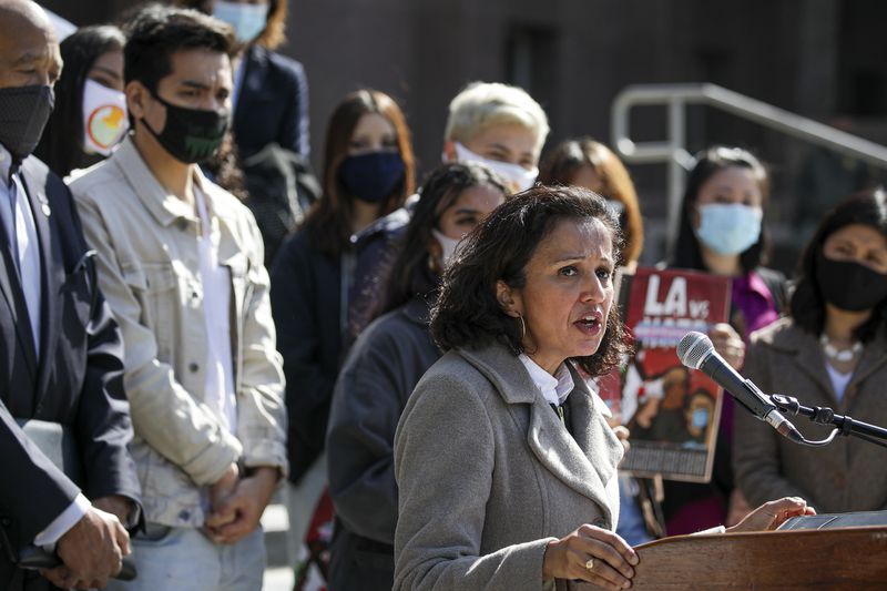 Manjusha Kulkarni speaks at a lectern, a crowd of people behind her.