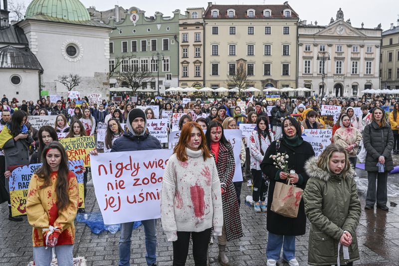 Ukrainian nationals and Poles painted in blood colors and holding banners stand silently in a city square in Krakow, Poland.