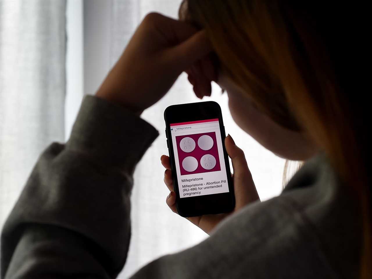 In this photo illustration, a person looks at an abortion pill displayed on a smartphone