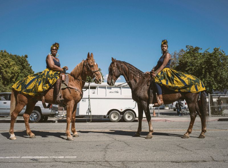 Two riders on horseback with print skirts that extend over the rumps of their horses.