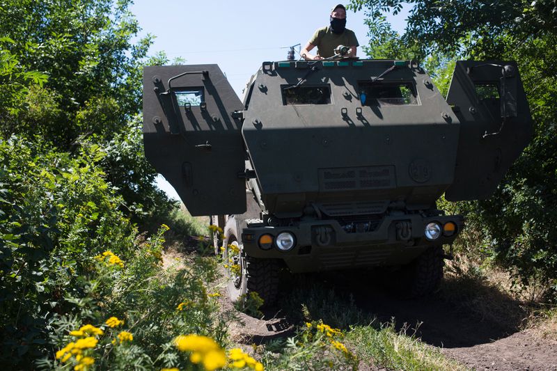 A tank-like truck driving through green bushes.