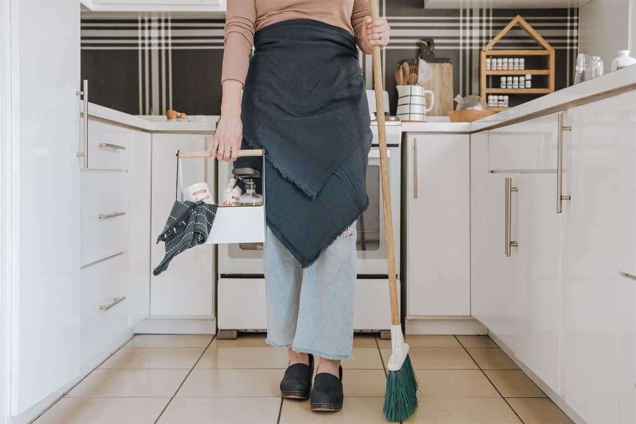 woman holding cleaning supplies and a broom in kitchen