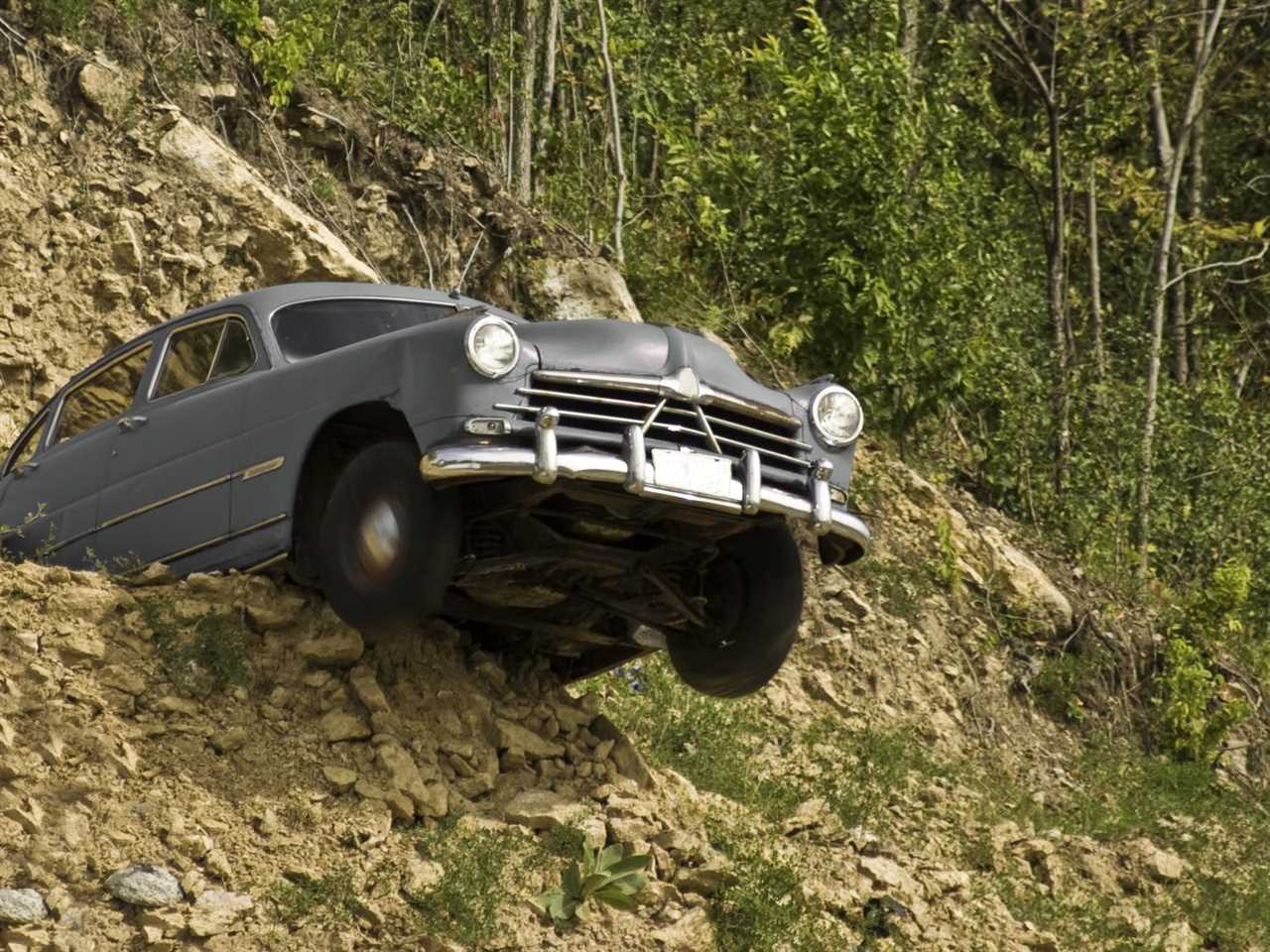 An older vehicle with its front half hanging off a cliff.