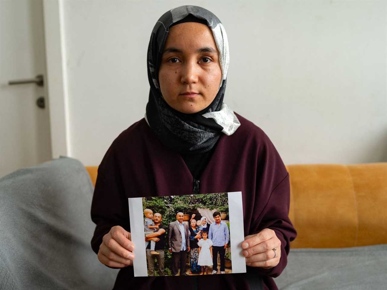 A woman wearing a headscarf sits on a couch and shows the camera a snapshot of her family.