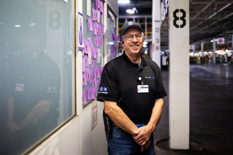 A man standing and smiling inside a car assembly plant.