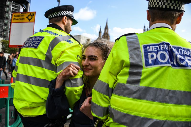 London police officers arrest a smiling Extinction Rebellion activist.