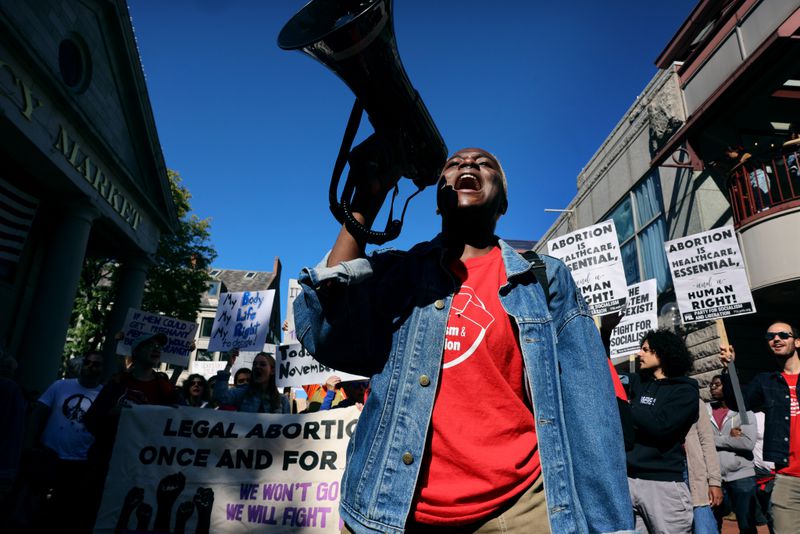 A person yelling into a megaphone while standing in front of fellow protesters carrying signs and banners in support of abortion as a human right.