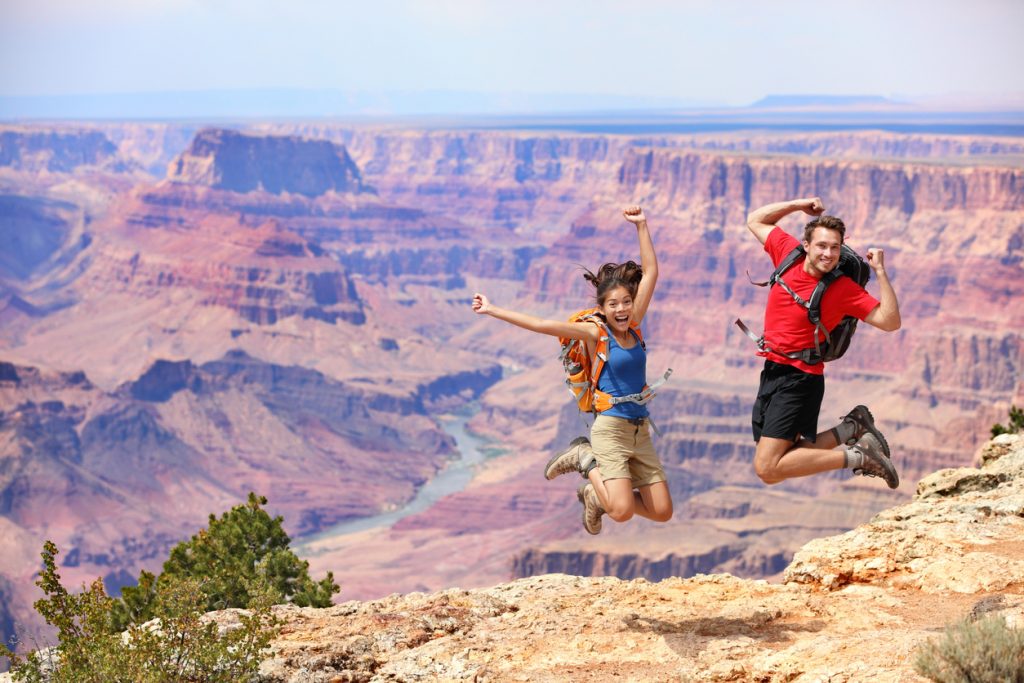 "Happy people jumping in Grand Canyon. Young multiethnic couple on hiking travel. Grand Canyon, south rim, Arizona, USA."
