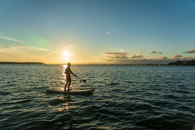 guy doing standup paddleboarding on sunset