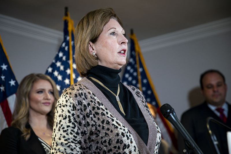 Power, in a leopard print sweater, her brown hair in a bob, speaks into a microphone, a row of US flags behind her.