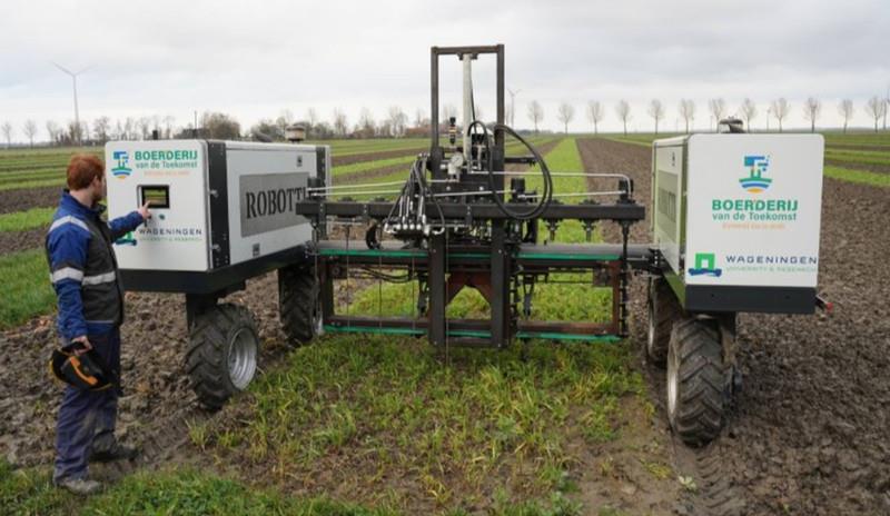 A large, high-tech tractor in a field with a technician pressing a touch-screen on the tractor.