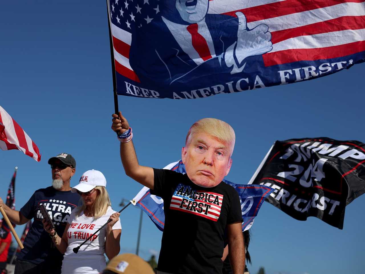 A person in a Trump mask waves an “America first” flag.