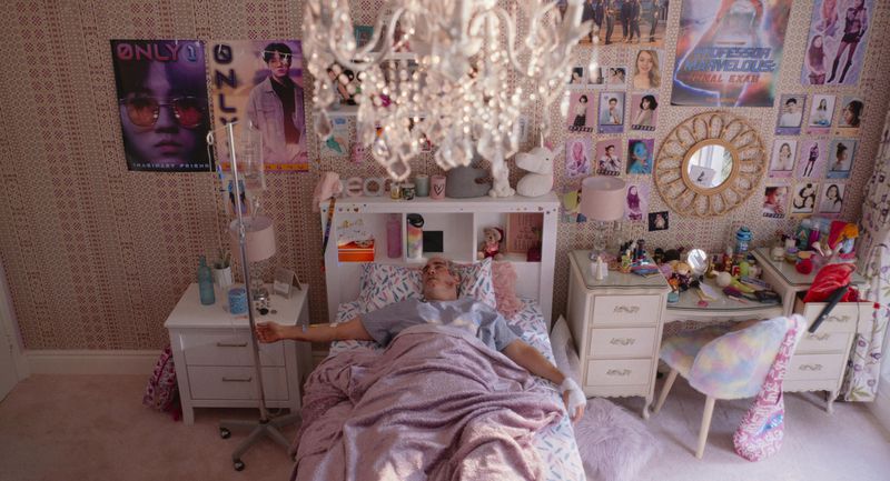 A middle-aged man in a bedroom with all kinds of posters on the walls, mostly for pop stars.