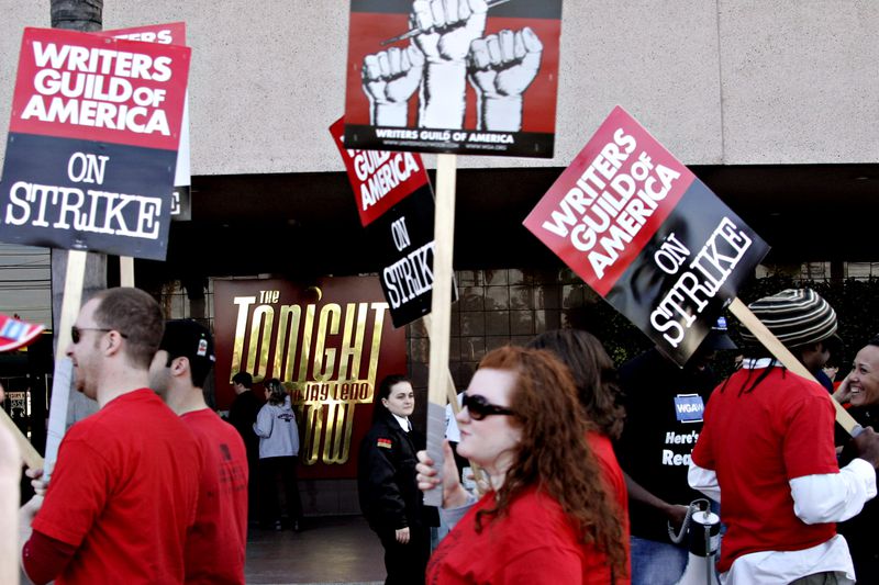 Picketers in red shirts holding Writers Guild signs protest on a Burbank, California, street.