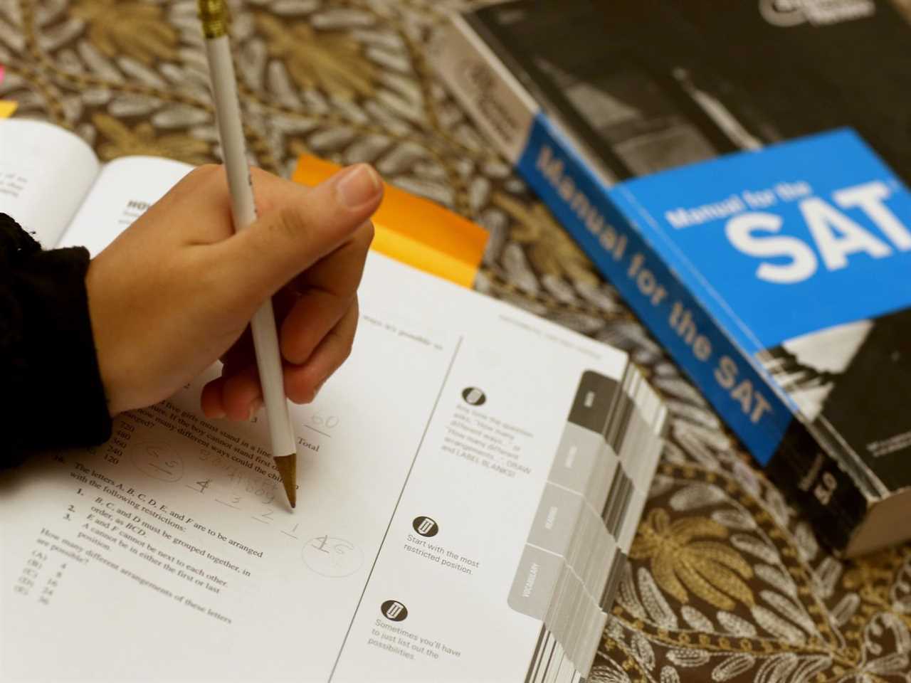 A hand holding a pencil over an SAT workbook. 