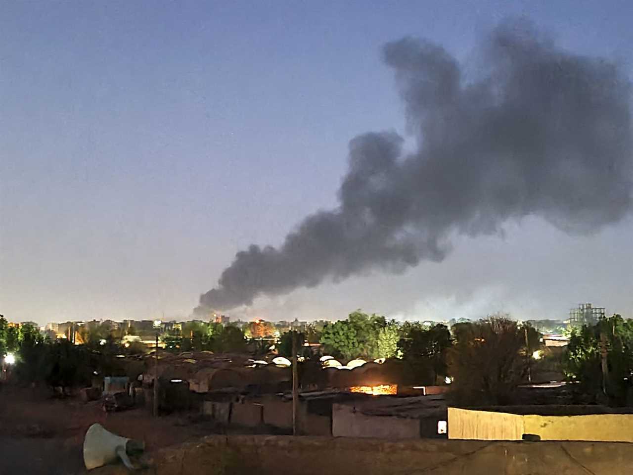 A large cloud of black smoke drifts across the Khartoum city skyline in Sudan, covering buildings, houses, and trees.