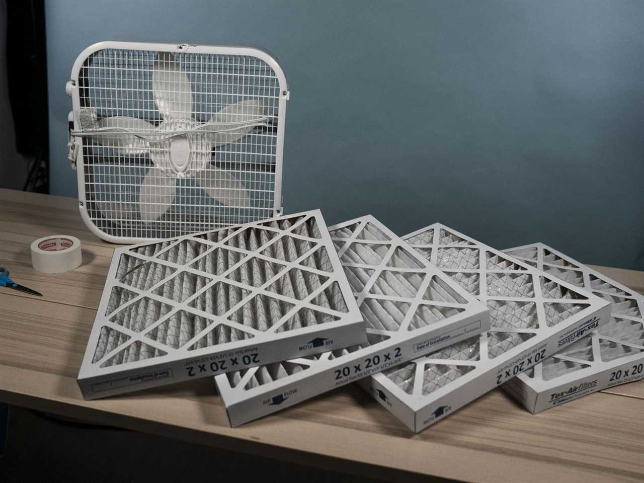 A box fan and several air filters sitting on a flat surface.