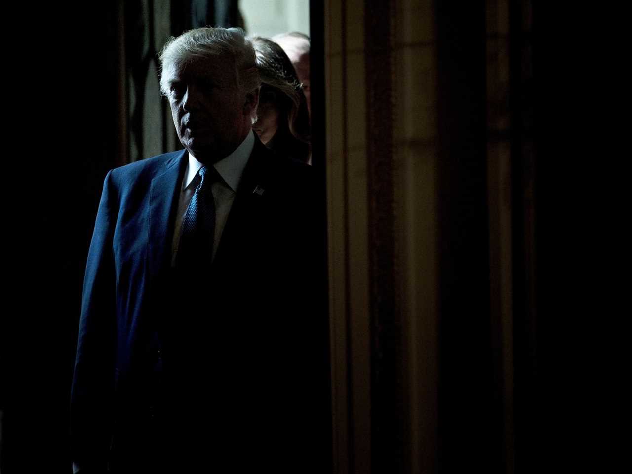 Donald Trump standing in the doorway of a dark room.