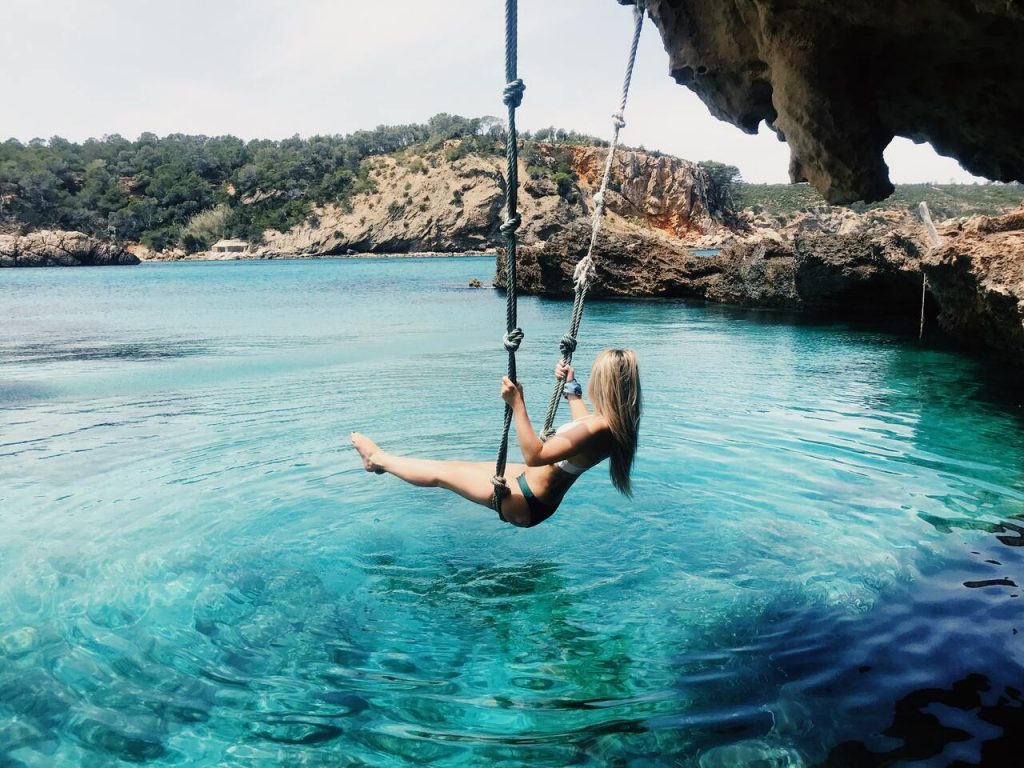 a girl on a swing on top of the water in playa cala xarraca, ibiza