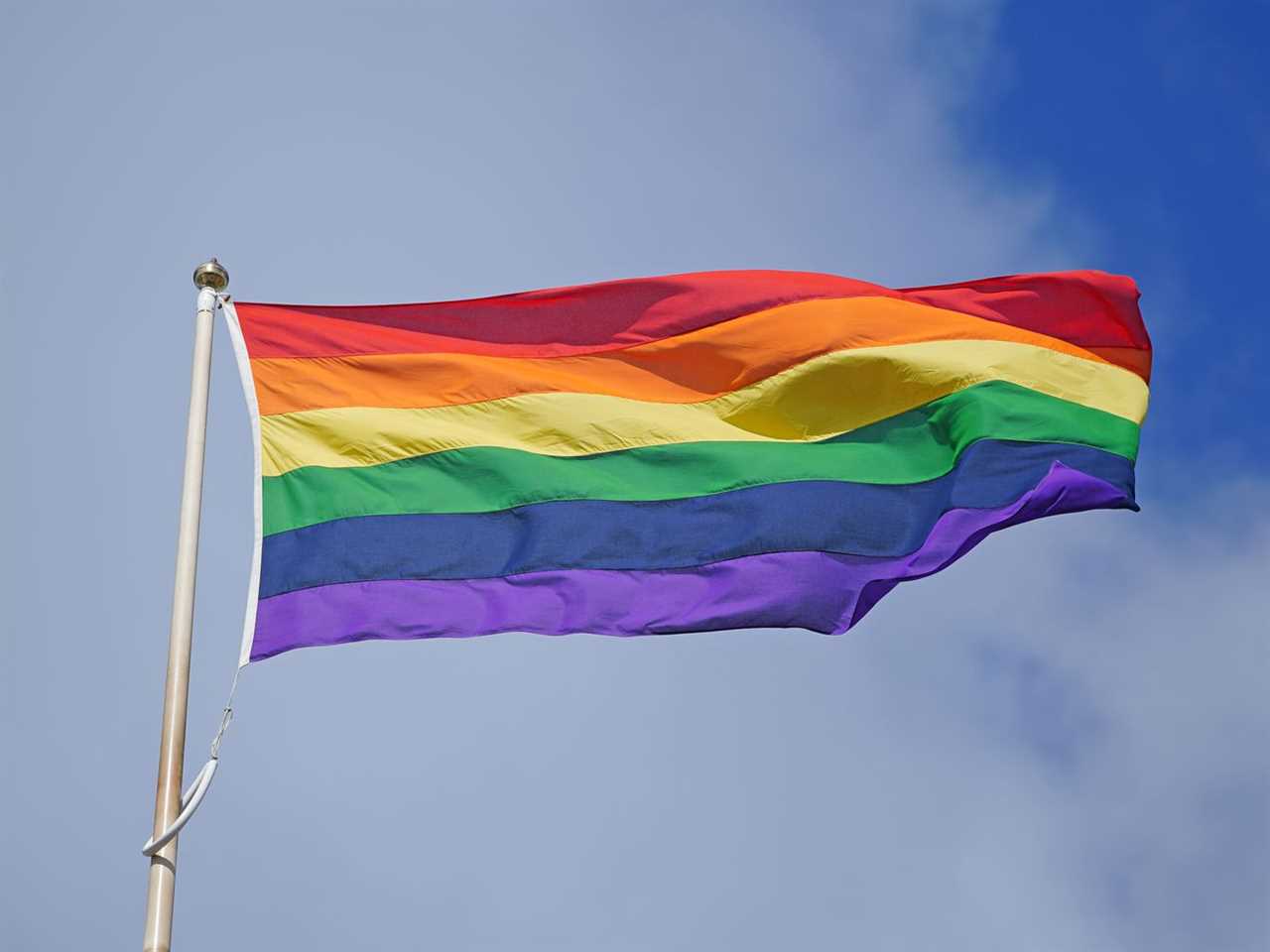 A Pride flag flies against a blue sky, in a 2023 Liverpool parade.