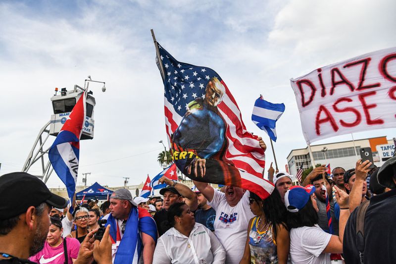 A Latino man in a Trump T-shirt raises a US flag emblazoned with an image of Trump dressed as Superman, a “T” on his chest in place of the comic book hero’s “S”. Other protesters are packed in around him, many holding Cuban flags.