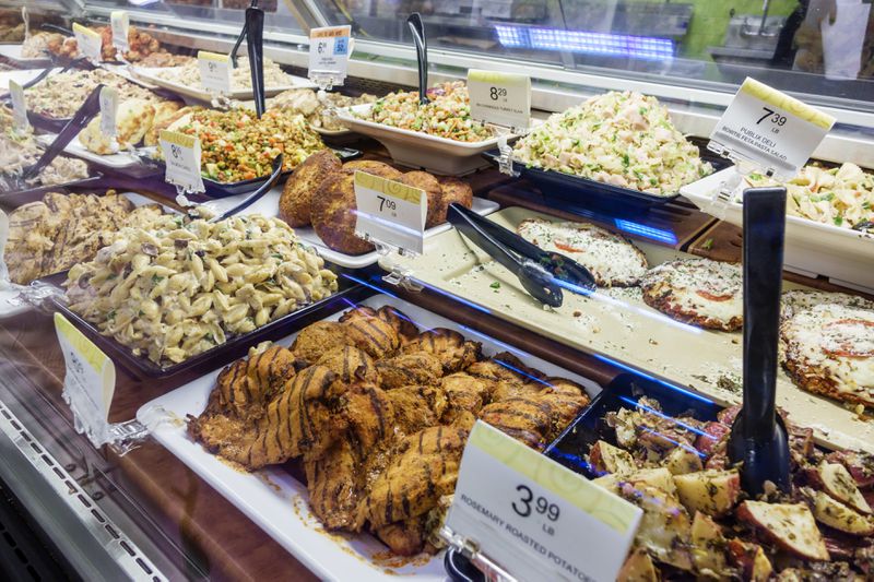 Grilled meats and potato salads behind a glass deli counter in a Publix.