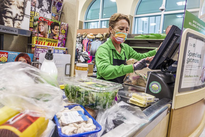 A woman in a mask checking out groceries at a checkout aisle. 