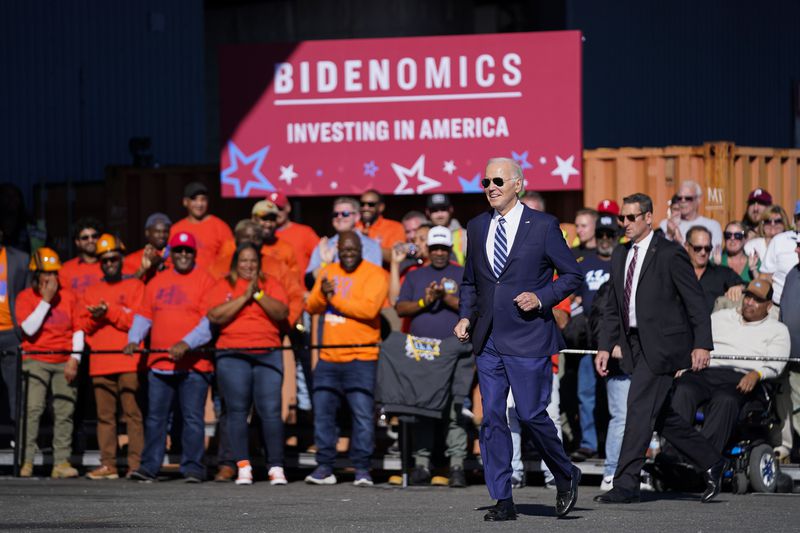 President Joe Biden walking in front of a crowd and a large banner that reads “Bidenomics, investing in America.”