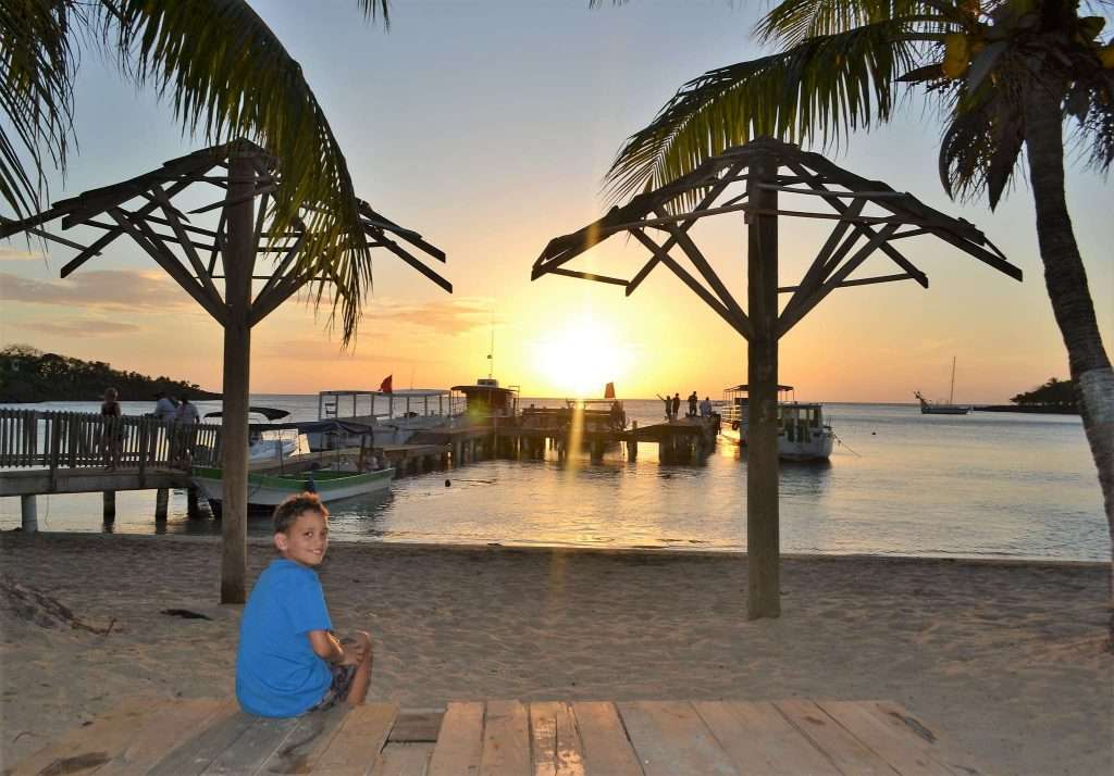 kid sitting in front of the beach in roatan honduras bay islands sunset