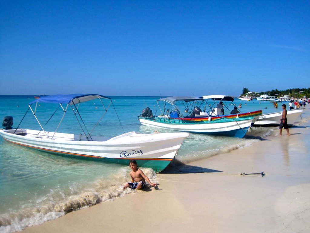 boats and a kid sitting on the sant in a beach at roatan honduras