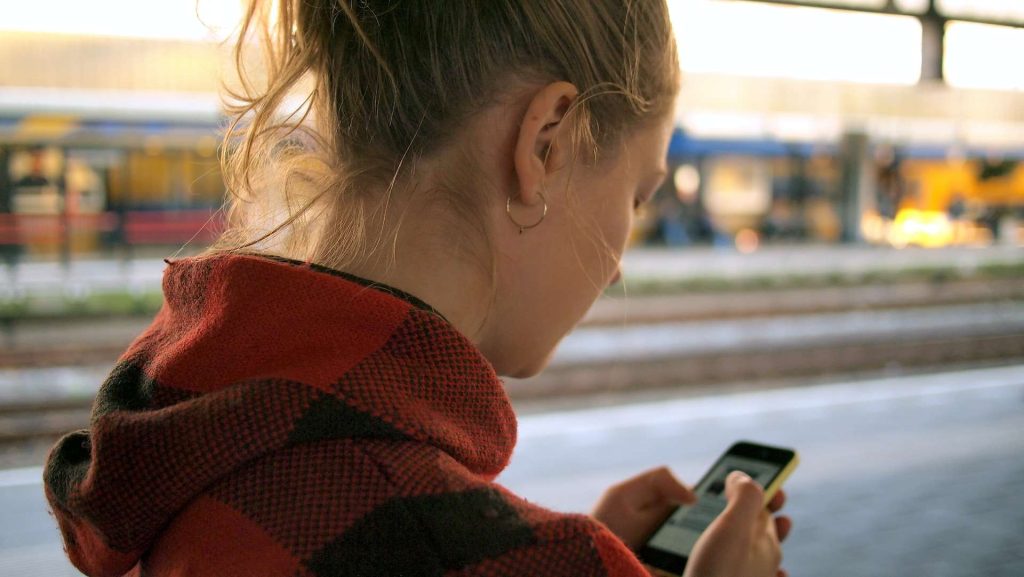 woman holding her phone at a train station while traveling and using an esim