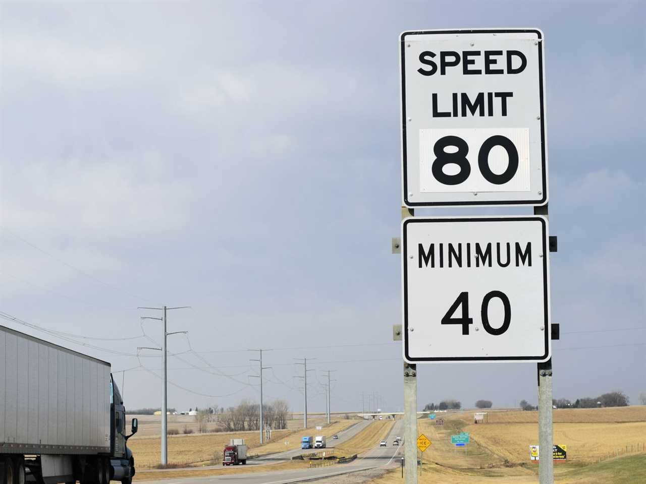 A photo of a trailer truck on a long flat highway passing a sign showing a speed limit minimum of 40 m.p.h. and maximum of 80 m.p.h.