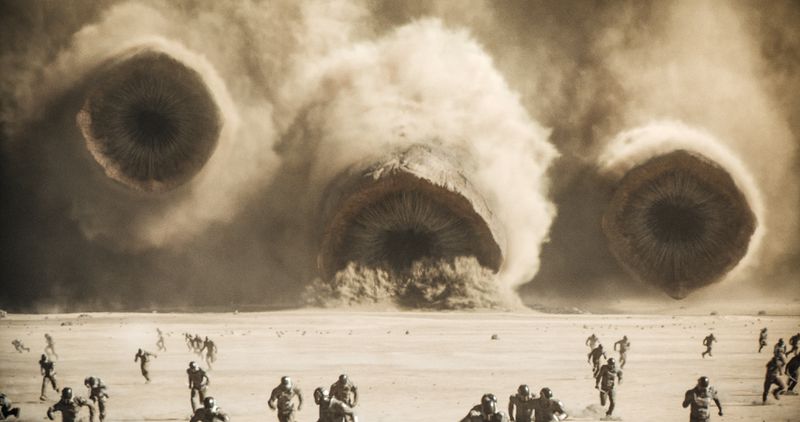 Three giant sandworms speed toward tiny fleeing soldiers.