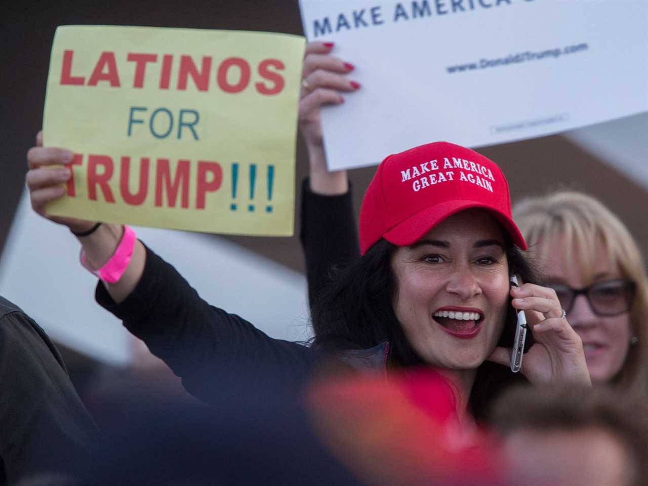 A woman in a MAGA hat holds a sign that says “Latinos for Trump!!!”