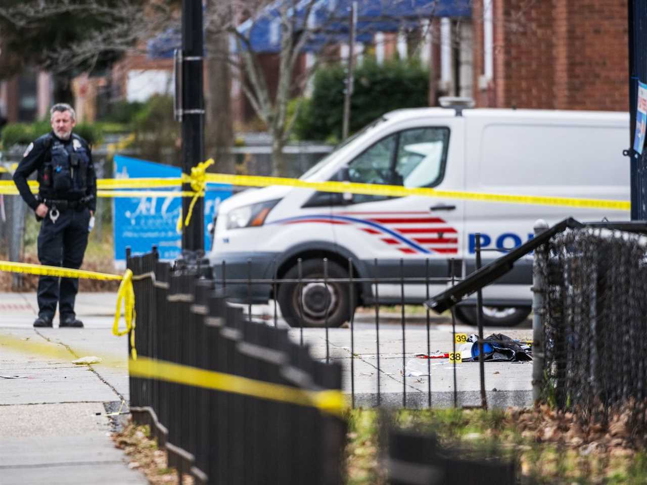 A police officer stands surrounded by caution tape. 