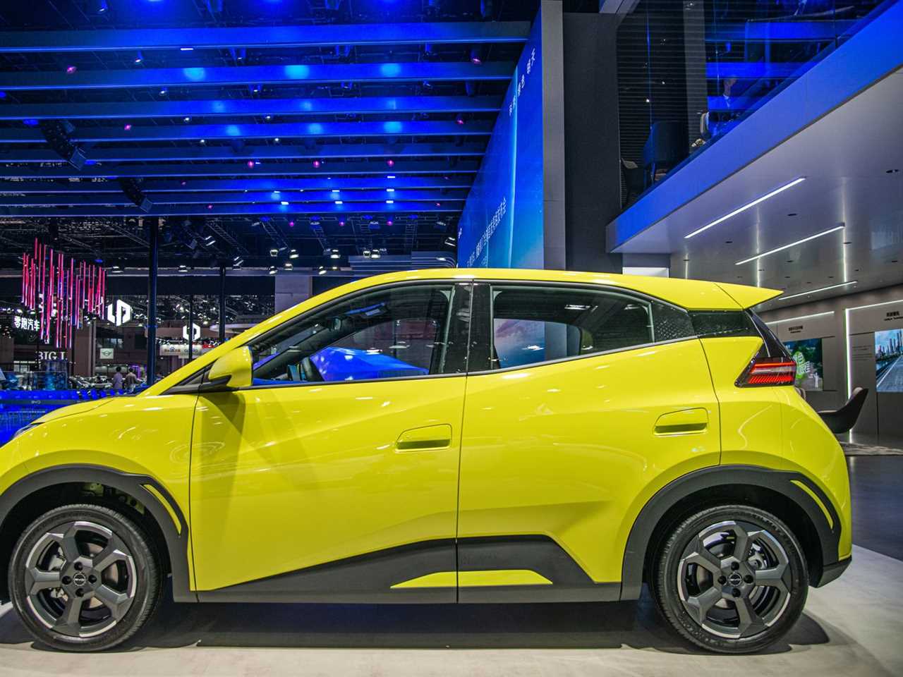 A squat yellow hybrid car on display in a large room with a high, blue-lit ceiling. 