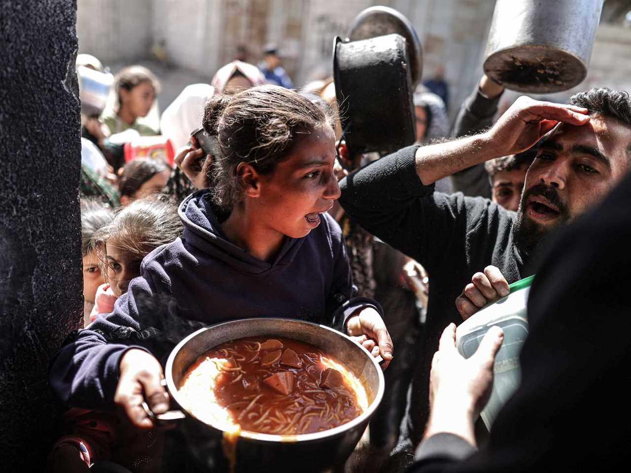 A girl holds a pot of food while being jostled by a crowd.