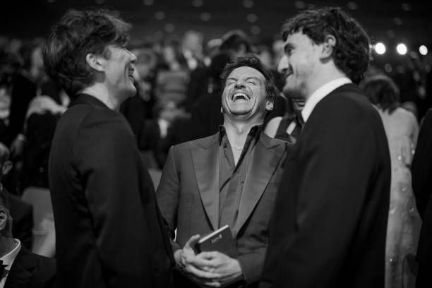 Three men in suits stand in a group and laugh.