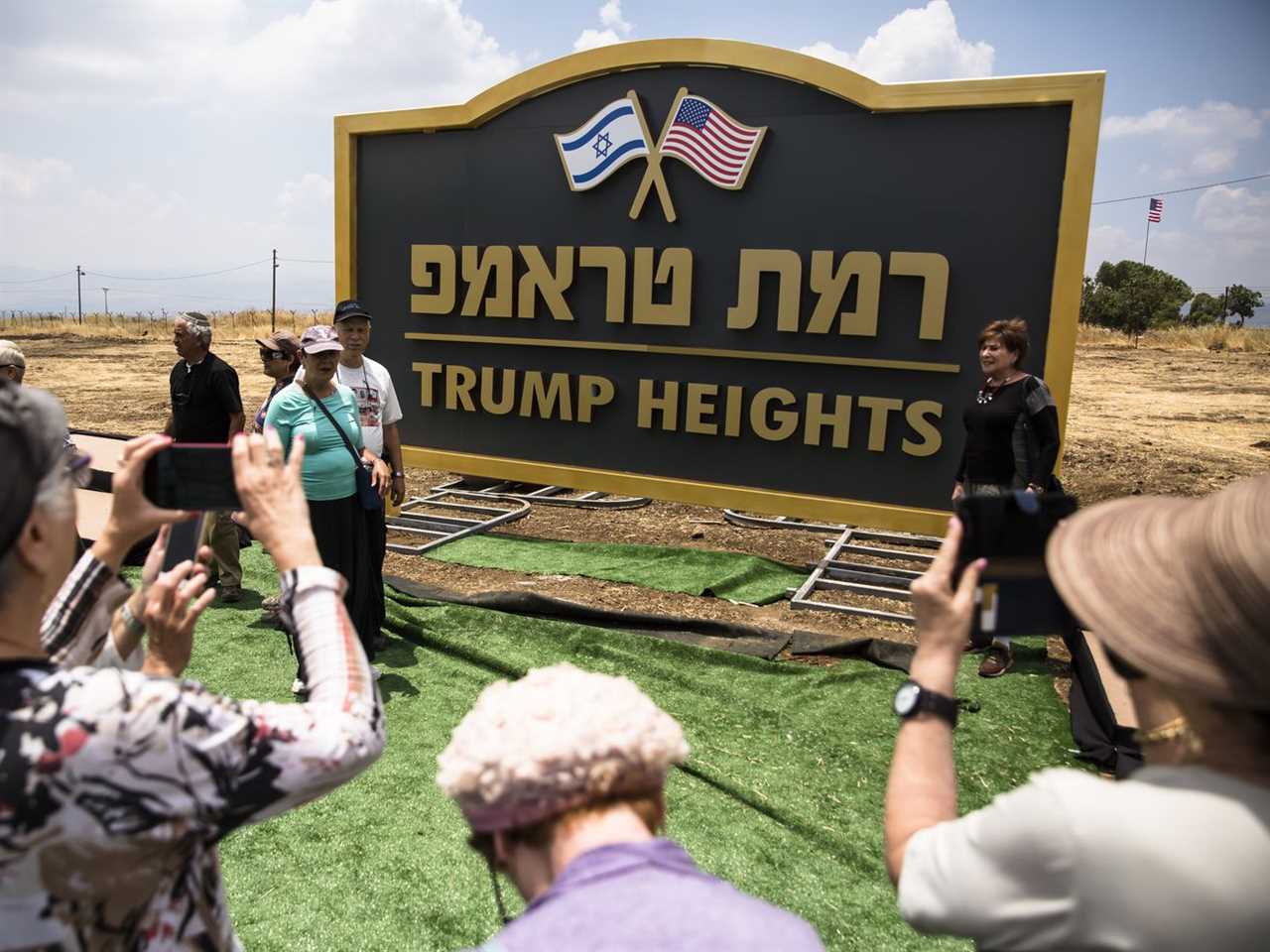 People take photos of a large sign with “Trump Heights” written in English underneath Hebrew writing and the US and Israel flags at the top.