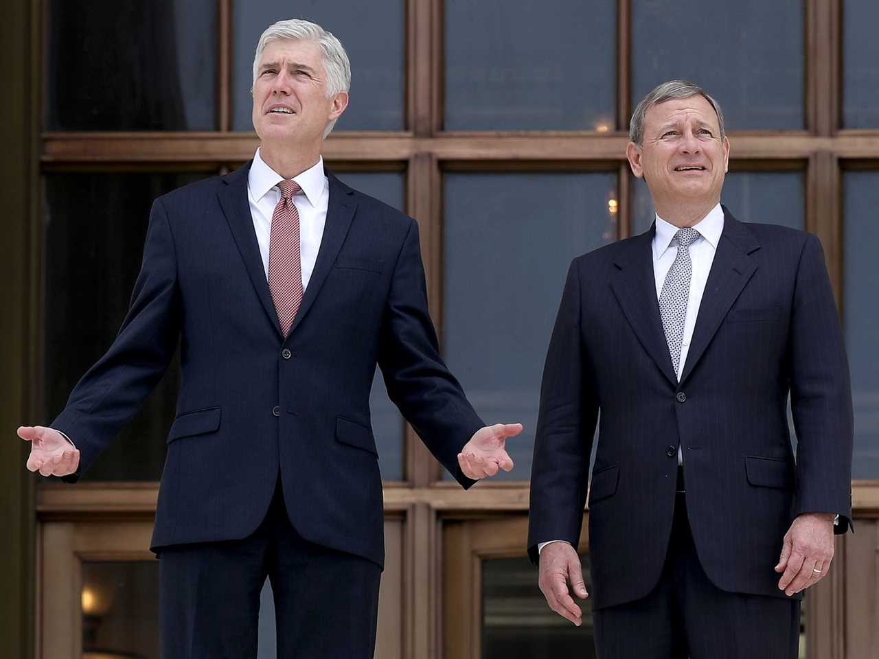 Justice Neil Gorsuch, left, in a navy suit and red tie, and Chief Justice John Roberts, right, in a black suit and gray tie, stand in front of the Supreme Court building.